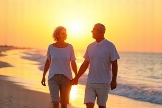 Happy senior couple walking on a beach at sunset, representing comfortable retirement.